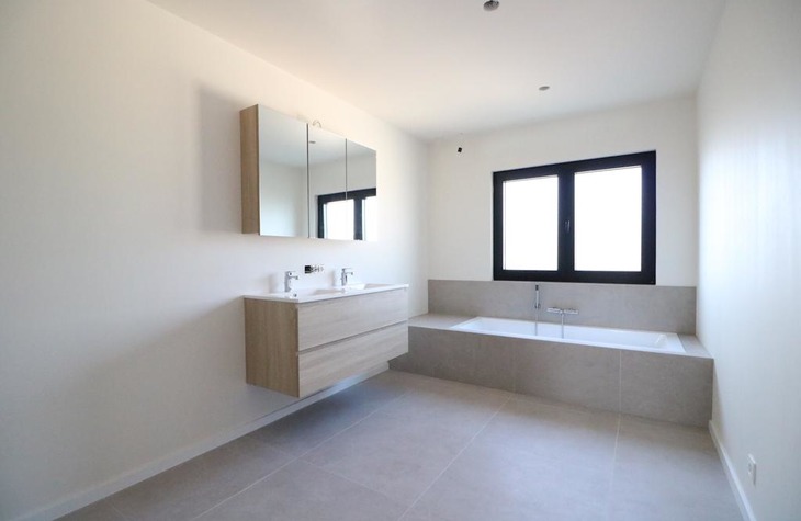 Moderne badkamer voorzien van een ruim bad en veel lichtinval dankzij het grote raam